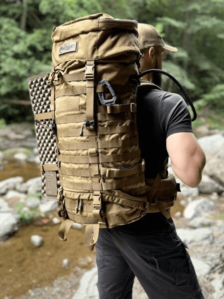 Ein Tourist mit großem Expeditionsrucksack an einem Gebirgsbach im Wald. Foto: Rigad
