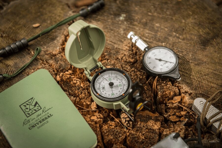 Kompass Ranger MK2 Helikon-Tex<sup>®</sup> und robustes Notizbuch auf einem Baumstumpf zur Orientierung in der Natur. Foto: Helikon-Tex, Rigad