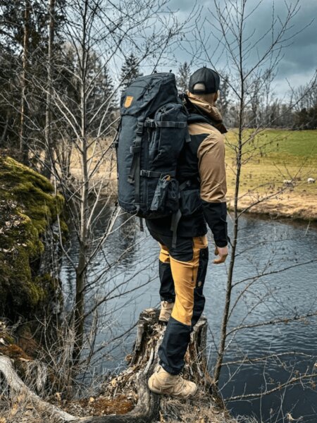 Outdoorhosen Fjällräven und Rucksack am Flussufer in der Natur. Foto: Rigad