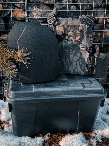 Zwei ballistische Platten vor dem Träger auf einer Transportkiste, Winterumgebung; Darstellung der Betriebs- und Lagerbedingungen.