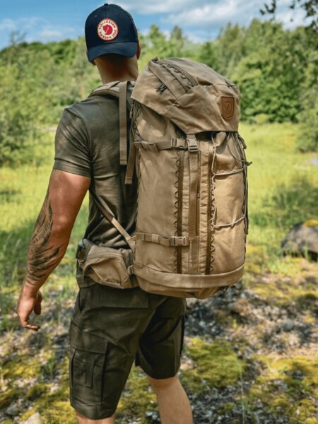 Ein Mann mit einem Fjällräven-Rucksack und -Basecap auf einer Sommertour als Schutz gegen Sonnenstich. Foto: Rigad