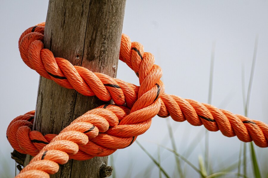 Ein starkes oranges Seil, das an einem Holzpfosten in einem einfachen Knoten gebunden ist