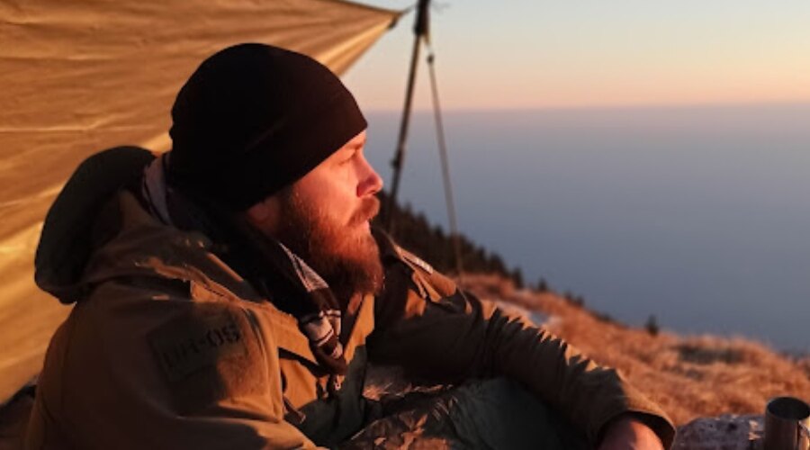 Ein Mann sitzt bei Sonnenuntergang und trägt eine Wintermütze Contact Fleece Beanie der Marke Snugpak.