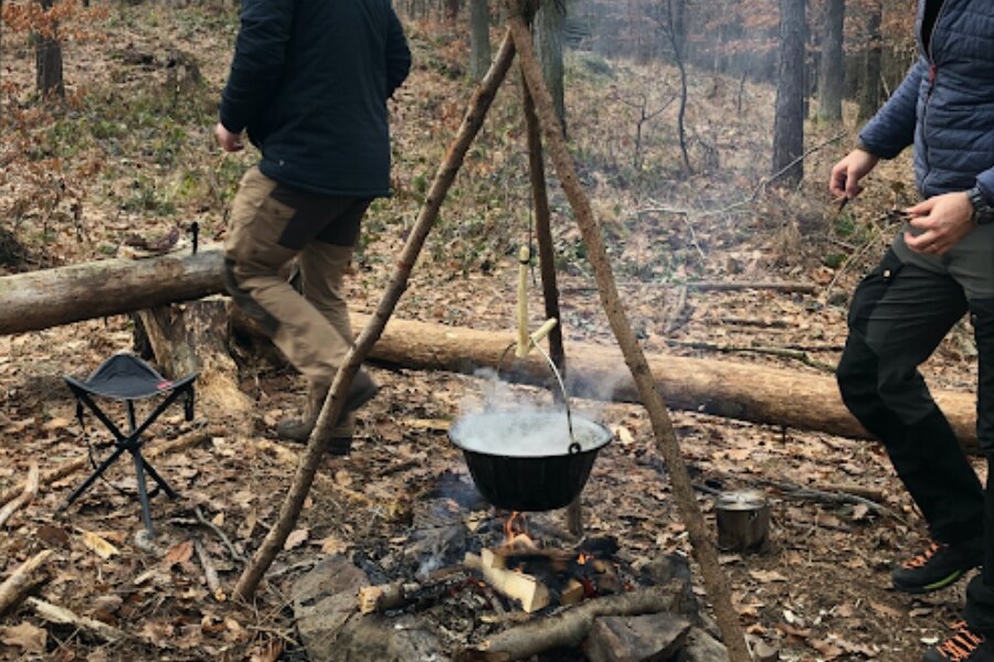 Ein Kessel zum Kochen, der an einem Gestell aus Ästen aufgehängt ist.