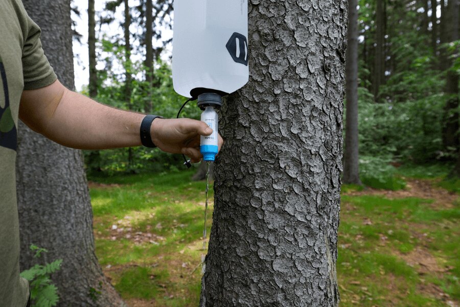 Ein Gravitationswasserfilter aufgehängt an einem Baum während der Wasserfiltration in der Natur. Foto: Rigad