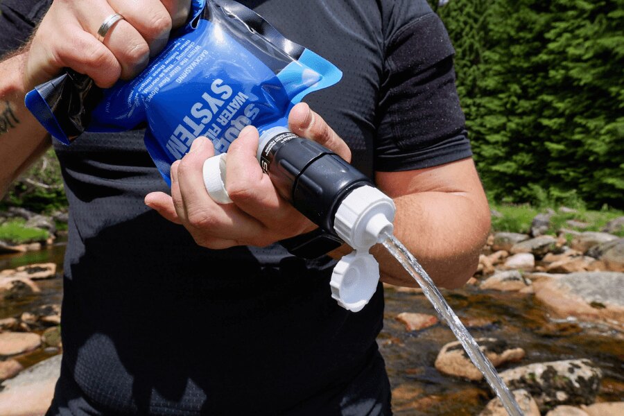 Die Person verwendet den Sawyer-Squeeze-Filter, um Wasser aus dem Beutel in der Natur zu drücken. Foto: Rigad