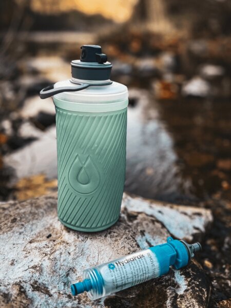 Faltflasche Flux™ HydraPak<sup>®</sup> mit aufgesetztem Wasserfilter HydraPak<sup>®</sup> (28 mm) auf einem Stein am Bach. Foto: Rigad