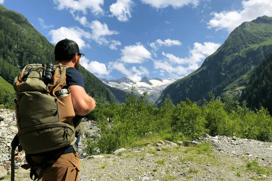 Ein Mann mit Rucksack und Thermoskanne in den Bergen. Quelle: Rigad