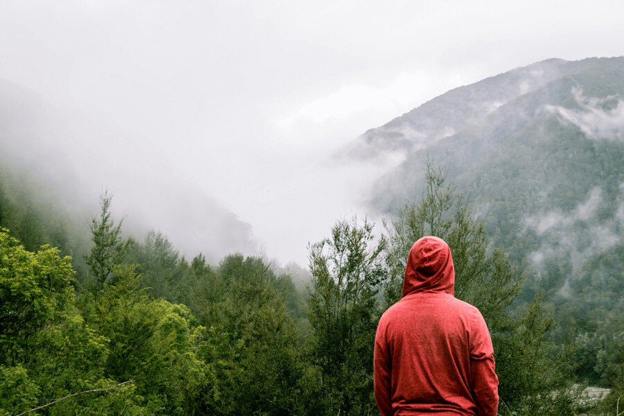 Ein Mann in einem roten Hoodie steht in den Bergen im Regen. Quelle: https://www.pexels.com/cs-cz/foto/395242/