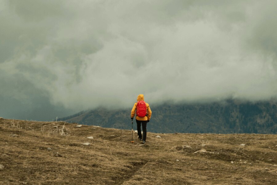 Ein Mann in einer gelben Jacke wandert im Regen in den Bergen. Quelle: pexels