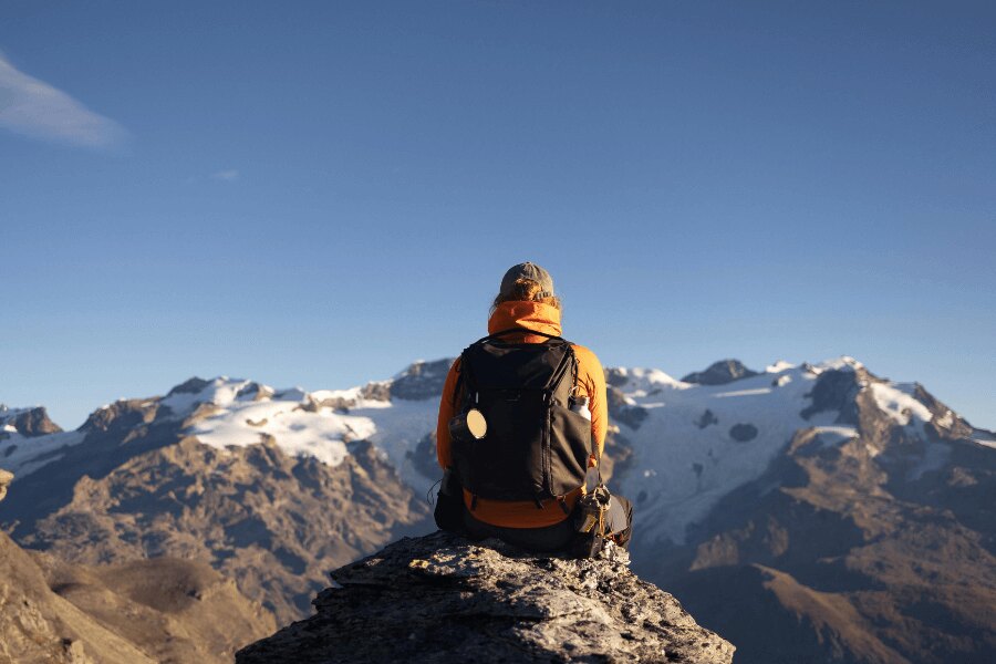Ein Mann in einer gelben Jacke mit einem Rucksack sitzt in den Bergen.