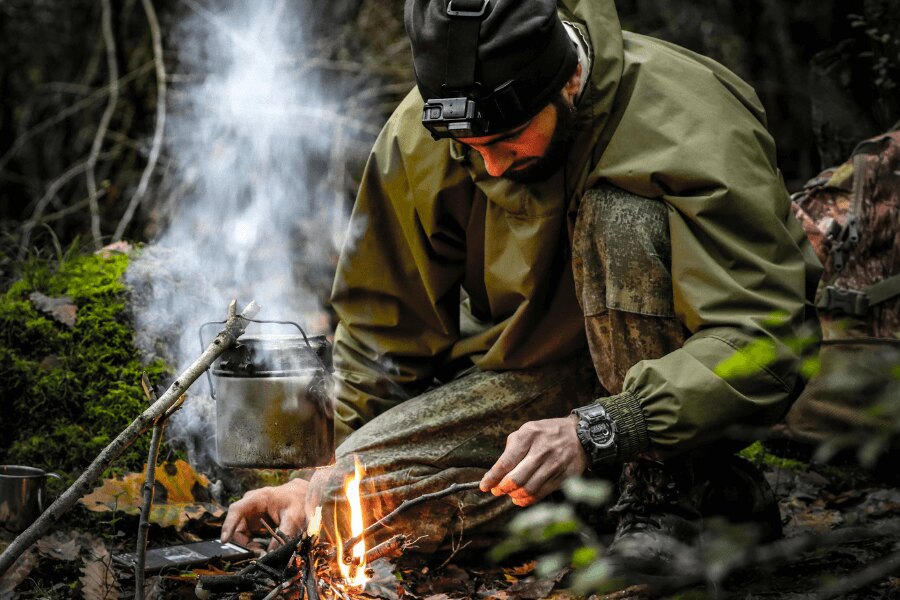 Mann in einer Membranjacke am Feuer im Wald.