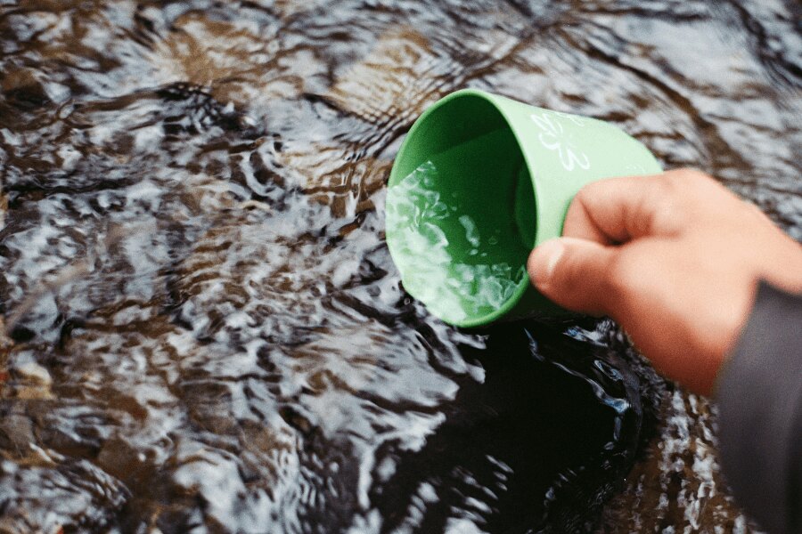 Wasser aus dem Bach in einen grünen Becher schöpfen.
