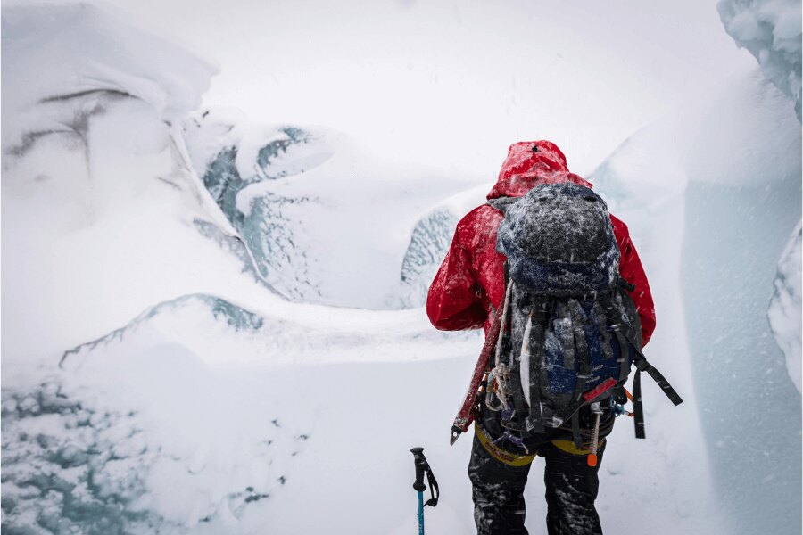 Ein Mann mit einem verschneiten Rucksack in eisiger Landschaft. Quelle: https://www.pexels.com/cs-cz/foto/ryma-studeny-snih-krajina-6730946/