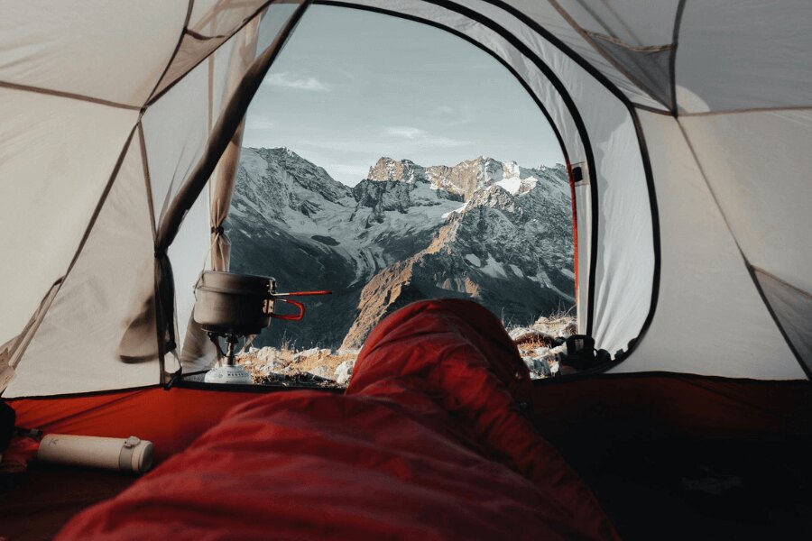 Der Blick aus dem roten Schlafsack auf die verschneiten Berge. Quelle: https://www.pexels.com/cs-cz/foto/krajina-hory-cestovani-dobrodruzstvi-9166687/