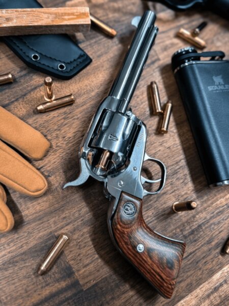 Einrevolver Ruger mit langem Lauf und Holzgriff, platziert zwischen Munition und Outdoor-Ausrüstung.
