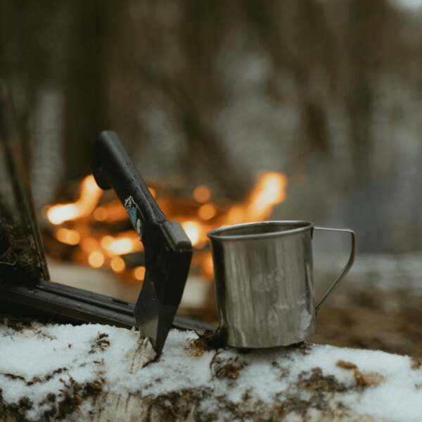 Bushcraft-Axt und Blechbecher im Wald am Feuer. Quelle: https://www.pexels.com/cs-cz/foto/ryma-studeny-snih-priroda-6204650/