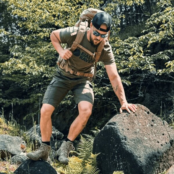 Ein Mann in funktioneller Outdoor-Bekleidung und mit einem Rucksack beim Aufstieg auf einen Felsen im Wald. Foto: Rigad
