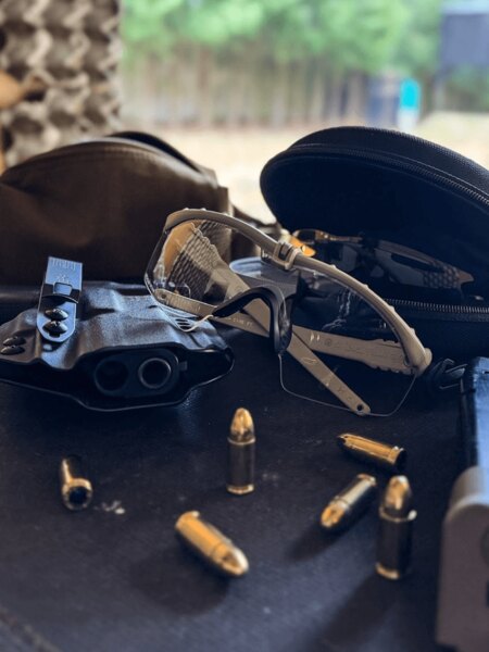 Schießbrille mit klarem Glas auf dem Tisch des Schießstands neben Munition und Zubehör; geeignet für Training und Kurse. Foto: Rigad