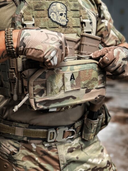 Ein Operator in einer Multicam-Ausrüstung öffnet das Pincer Admin Panel Agilite<sup>®</sup>, das an einem K-ZERO SF Plattenträger befestigt ist, und hantiert mit Magazinen. Foto: Rigad