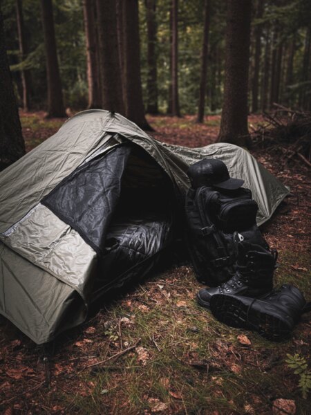 Biwaksack Snugpak mit ausgebreitetem Schlafsack, daneben Rucksack und Winterstiefel, bereit für eine Notübernachtung in der Natur. Foto: Rigad