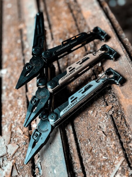 Drei Multitools Leatherman Signal in verschiedenen Farbvarianten auf einer Holzoberfläche platziert.