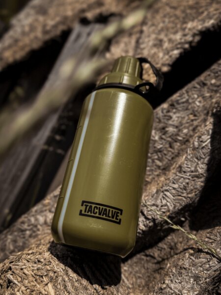 TacValve<sup>®</sup> ModCan-Feldflasche in Grün auf einem Holzuntergrund in einer Outdoor-Umgebung.