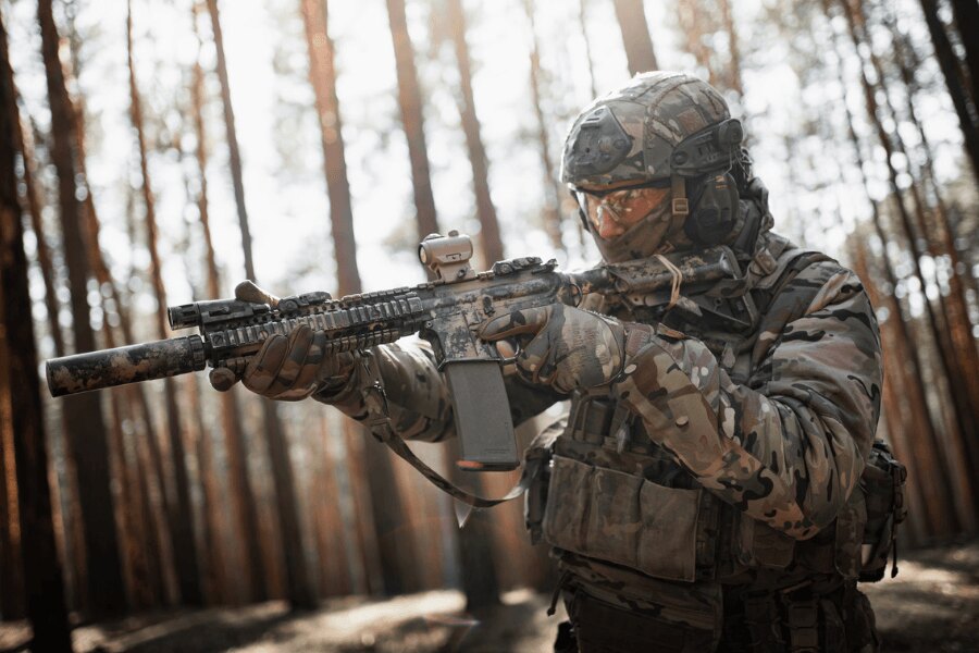 Modernes Gewehr AR-15 mit Rotpunktvisier und Schalldämpfer beim Schießen in einer Waldumgebung.