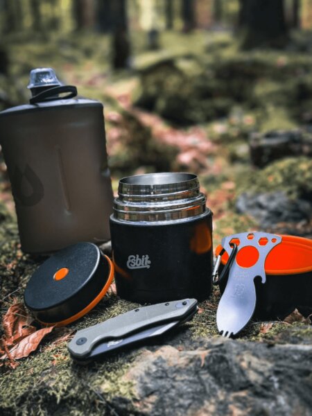 Offene Thermo-Essensbehälter von Esbit mit Outdoor-Flasche, Klappmesser und Besteck im Wald.