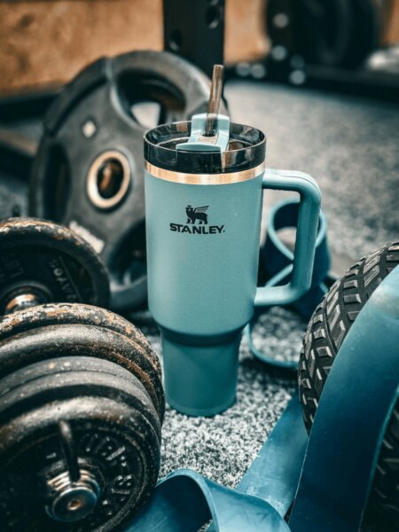 Stanley-Thermobecher mit Strohhalm, abgelegt zwischen Hanteln und Fitnessgeräten.