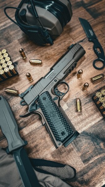 Pistole Schmeisser HUGO 1911 5" im Kaliber .45 ACP auf dem Tisch gelegt mit Munition und Schießausrüstung.