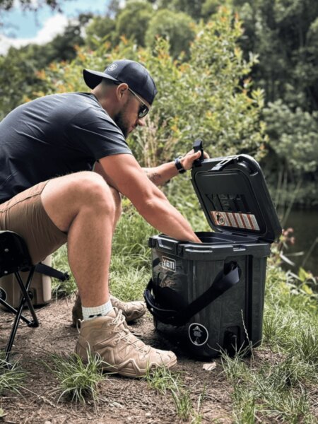 Der Mann öffnet die Transportbox YETI LoadOut GoBox am Wasser.