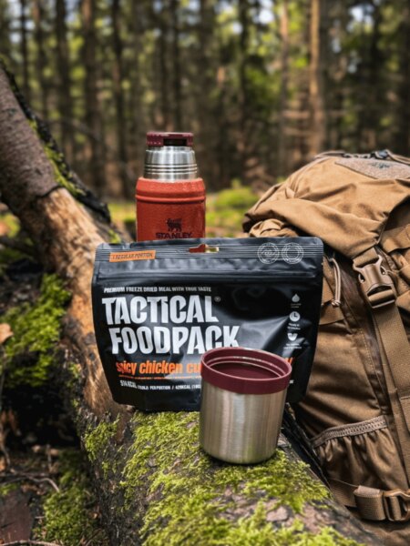 Gefriergetrocknetes Essen von Tactical Foodpack mit Thermoskanne Stanley, Tasse und Rucksack im Wald.