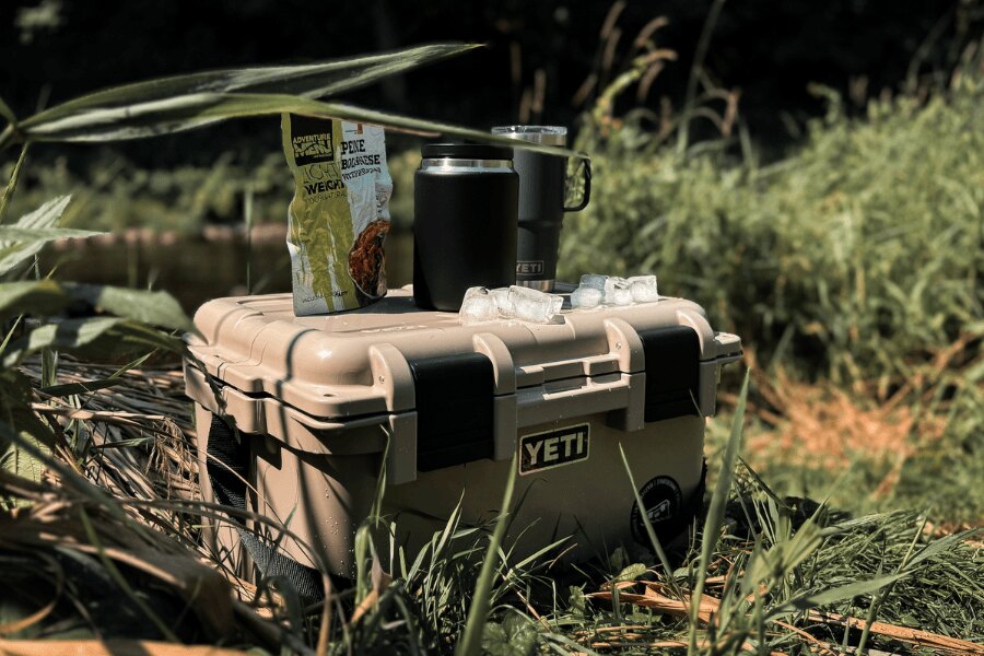Transportbox YETI LoadOut GoBox mit verpacktem Essen und Thermobechern in der Natur.