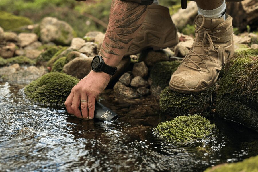 Wasser aus einem Waldbach in eine Yeti-Flasche füllen.