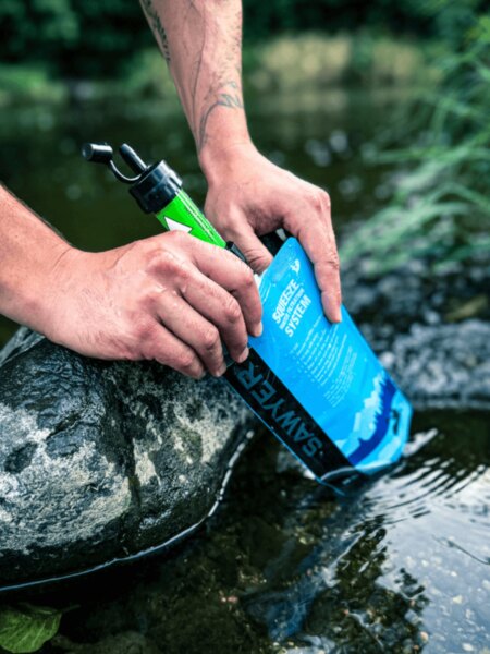 Wasserfiltration mit einem Sawyer-Filter, der an einem faltbaren Beutel befestigt ist.